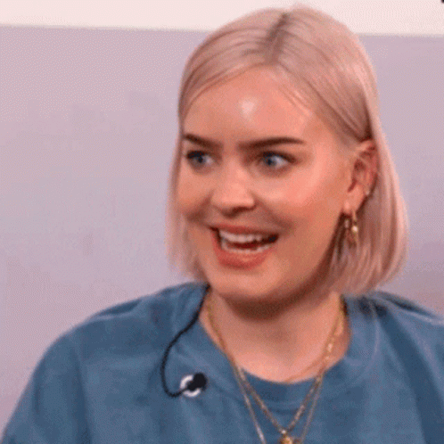 A Woman With Blonde Hair Is Wearing A Blue Shirt And Smiling . GIF