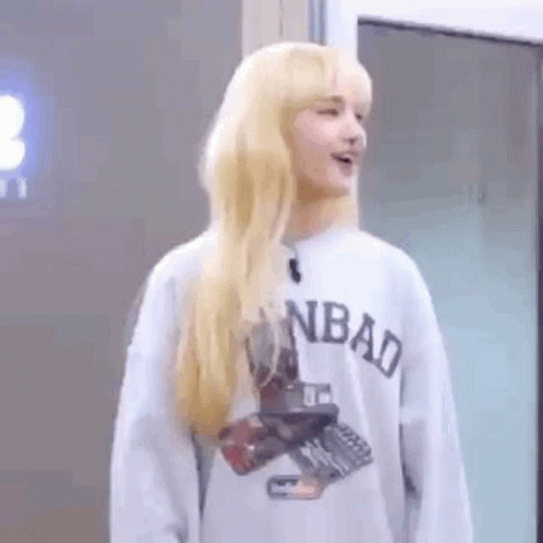 A Woman With Blonde Hair Is Wearing A Gray Sweatshirt And Standing In Front Of A Door . GIF