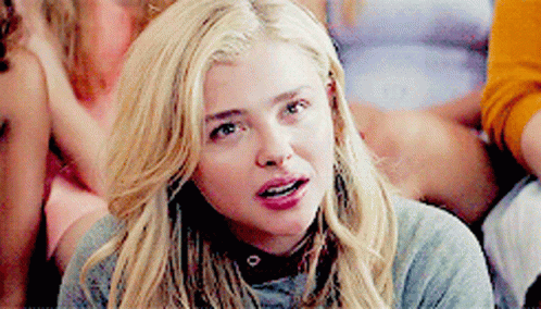 A Woman With Blonde Hair Is Wearing A Grey Sweater And Choker . GIF