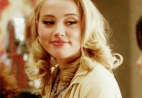 A Woman With Blonde Hair Is Wearing A Tan Jacket And A Necklace GIF