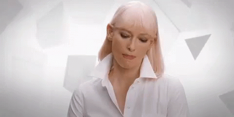 A Woman With Blonde Hair Is Wearing A White Shirt And Making A Funny Face . GIF