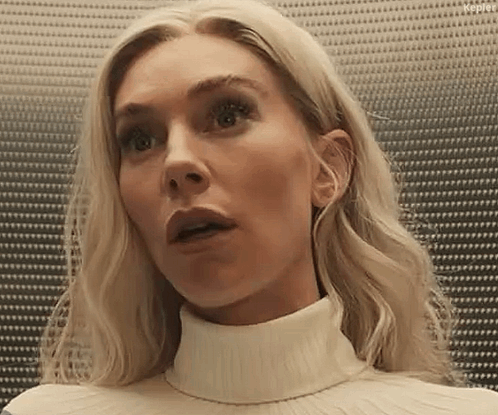 A Woman With Blonde Hair Is Wearing A White Turtleneck Sweater And Looking Surprised . GIF