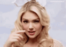A Woman With Blonde Hair Is Wearing Bunny Ears And Pointing To Her Face . GIF