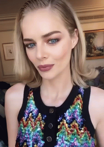 A Woman With Blue Eyes Is Wearing A Sequined Top With Buttons GIF