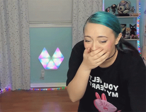 A Woman With Blue Hair Is Covering Her Mouth With Her Hand And Wearing A Black T-Shirt With A Rabbit On It GIF