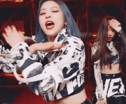A Woman With Blue Hair Is Dancing With Another Woman In A Crop Top On A Stage . GIF