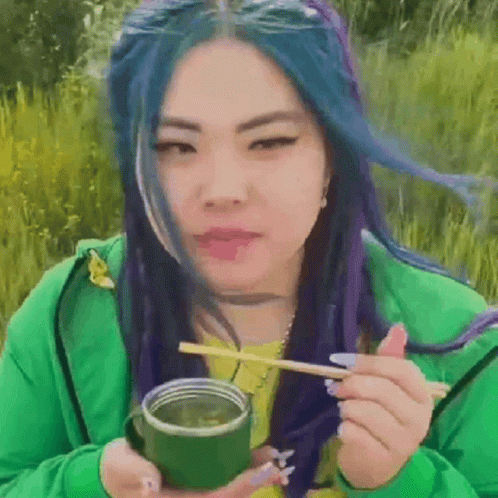 A Woman With Blue Hair Is Holding A Green Cup And Chopsticks . GIF