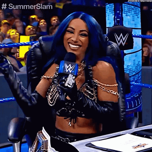 A Woman With Blue Hair Is Holding A Microphone And Smiling While Sitting In A Chair . GIF