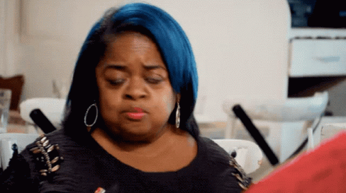 A Woman With Blue Hair Is Sitting At A Table Looking At A Piece Of Paper GIF