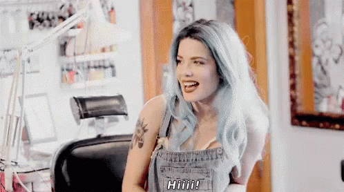 A Woman With Blue Hair Is Sitting In A Chair With Her Mouth Open And A Tattoo On Her Arm . GIF