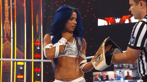 a woman with blue hair is standing in a wrestling ring holding a championship belt and talking to a referee .