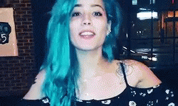 A Woman With Blue Hair Is Standing In Front Of A Brick Wall And Smiling . GIF
