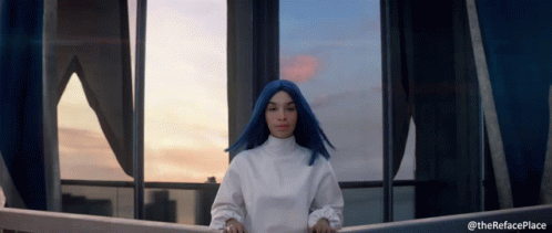 A Woman With Blue Hair Is Standing In Front Of A Window With The Words " Therefaceplace " Below Her GIF