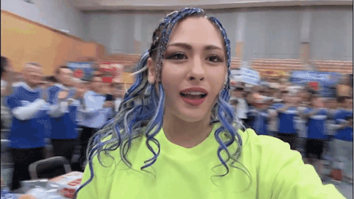 A Woman With Blue Hair Is Taking A Selfie In Front Of A Crowd . GIF