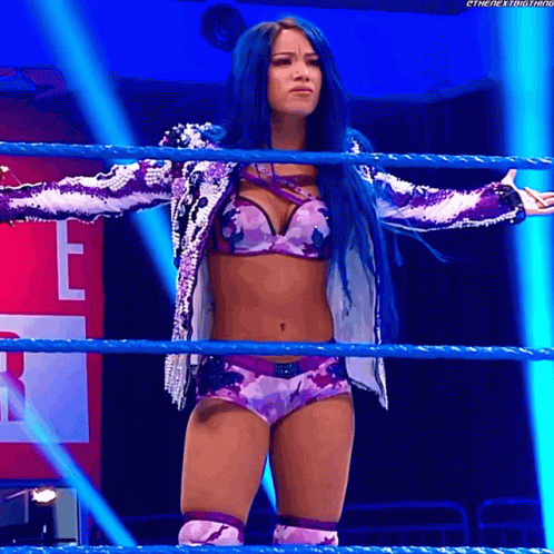 A Woman With Blue Hair Stands In A Wrestling Ring With Her Arms Outstretched GIF