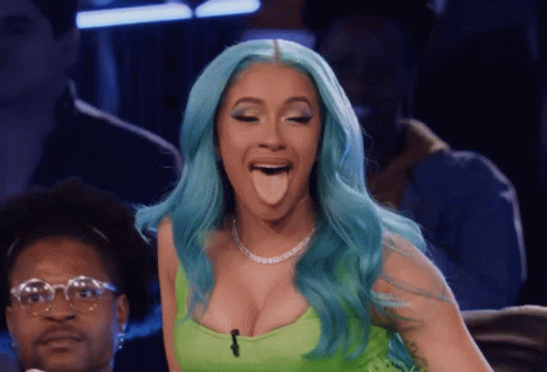 A Woman With Blue Hair Sticking Her Tongue Out While Wearing A Green Top GIF