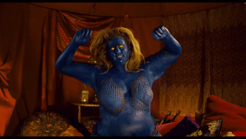 A Woman With Blue Paint On Her Face And Body Is Flexing Her Muscles GIF
