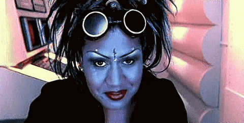 A Woman With Blue Paint On Her Face And Goggles On Her Head Looks At The Camera . GIF