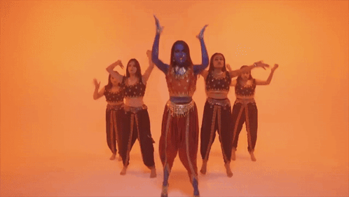 A Woman With Blue Paint On Her Face Is Kneeling In Front Of A Group Of Dancers GIF