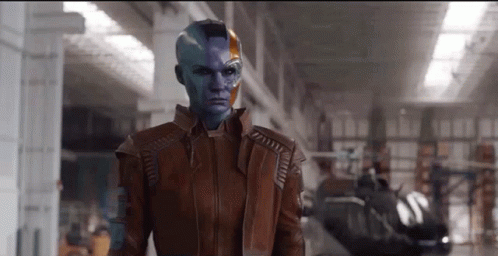 A Woman With Blue Paint On Her Face Is Wearing A Brown Jacket And Standing In A Warehouse . GIF