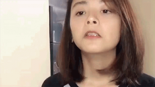 A Woman With Braces On Her Teeth Is Making A Funny Face While Standing In Front Of A Refrigerator . GIF