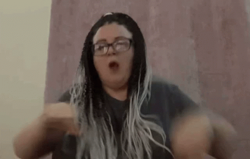 A Woman With Braids And Glasses Is Making A Funny Face With Her Hands In The Air . GIF