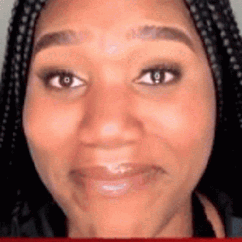 A Woman With Braids Is Smiling And Looking At The Camera . GIF