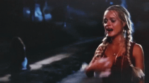 A Woman With Braids Is Standing On A Street At Night GIF