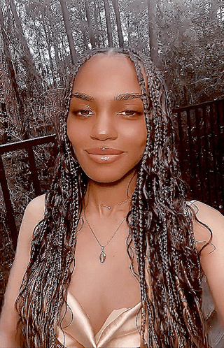 A Woman With Braids Is Wearing A Gold Top And A Necklace With The Letter O On It GIF