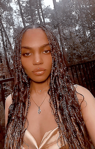 A Woman With Braids Is Wearing A Necklace And A Gold Top GIF