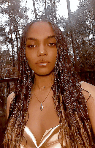 A Woman With Braids Is Wearing A Necklace And A Gold Top GIF