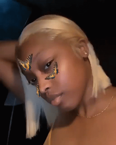 A Woman With Butterflies Painted On Her Face Looks At The Camera GIF