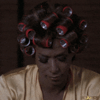 A Woman With Curlers On Her Head Is Wearing A Gold Shirt GIF