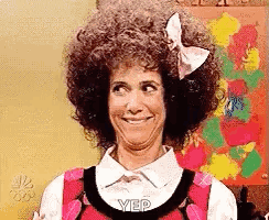 A Woman With Curly Hair And A Bow On Her Head Is Smiling And Making A Funny Face . GIF