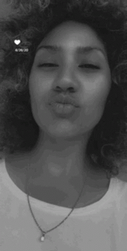 A Woman With Curly Hair And A Necklace Is Blowing A Kiss . GIF