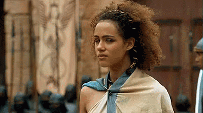A Woman With Curly Hair And A Scarf Around Her Neck Is Standing In Front Of A Door . GIF