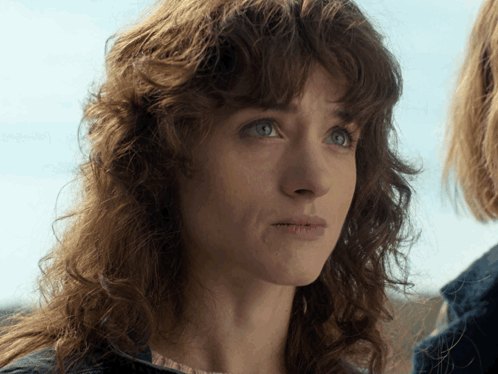 A Woman With Curly Hair And Blue Eyes Looks At The Camera GIF