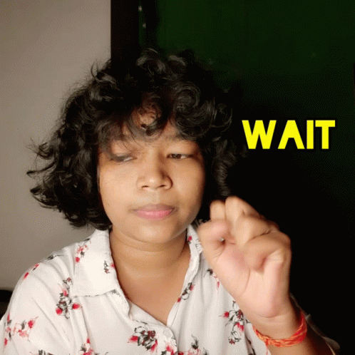 A Woman With Curly Hair Holds Her Hand Up In Front Of A Sign That Says " Wait " GIF