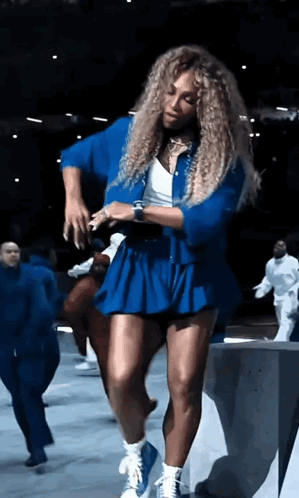 A Woman With Curly Hair Is Dancing In A Blue Dress GIF