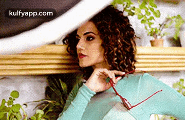 A Woman With Curly Hair Is Holding A Pair Of Glasses In Her Hand . GIF