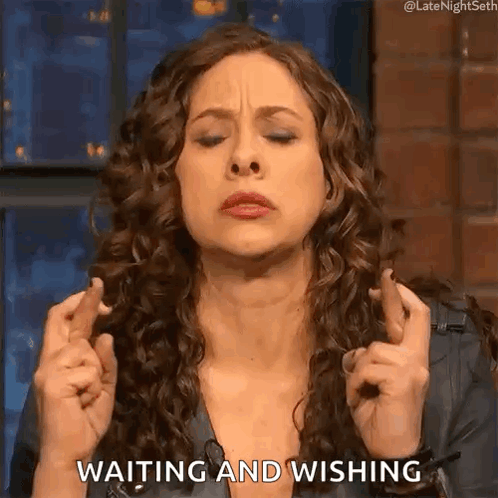 A Woman With Curly Hair Is Holding Her Fingers Crossed And Saying Waiting And Wishing . GIF