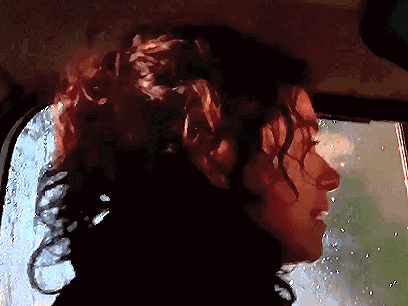 A Woman With Curly Hair Is Looking Out A Window GIF
