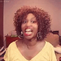 A Woman With Curly Hair Is Making A Funny Face While Wearing A Yellow Shirt And Earrings . GIF