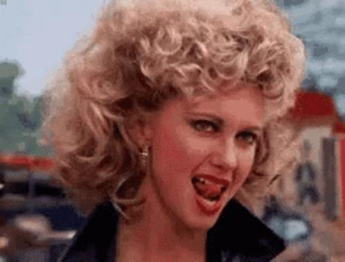 A Woman With Curly Hair Is Making A Funny Face With Her Tongue Hanging Out . GIF