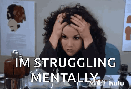 A Woman With Curly Hair Is Sitting At A Desk With Her Hands On Her Head And The Words Im Struggling Mentally GIF