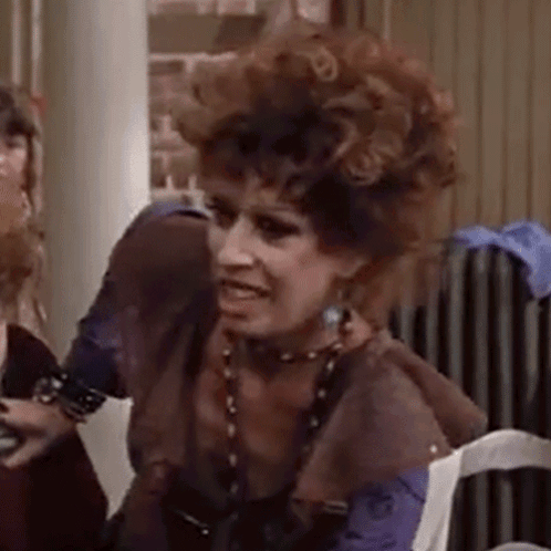 A Woman With Curly Hair Is Sitting In A Chair And Making A Face . GIF