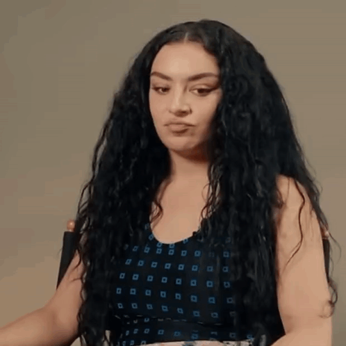 A Woman With Curly Hair Is Sitting In A Chair And Making A Funny Face . GIF