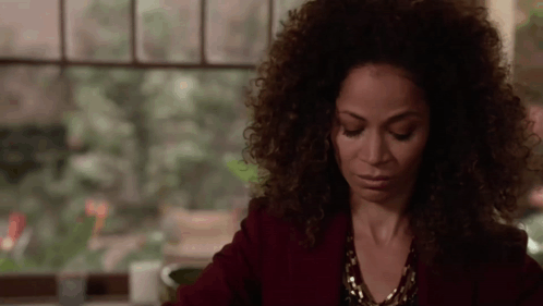 A Woman With Curly Hair Is Sitting In Front Of A Window With Her Eyes Closed . GIF