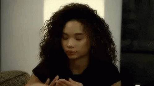 a woman with curly hair is sitting on a couch with her eyes closed and her hands on her face .