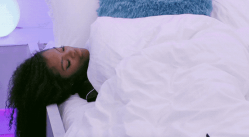 A Woman With Curly Hair Is Sleeping In A Bed With A White Blanket GIF